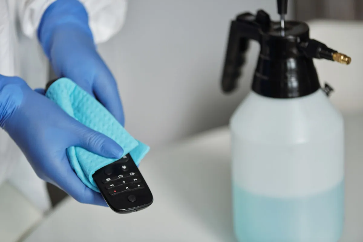 Gloved hands disinfecting a remote control with a cloth