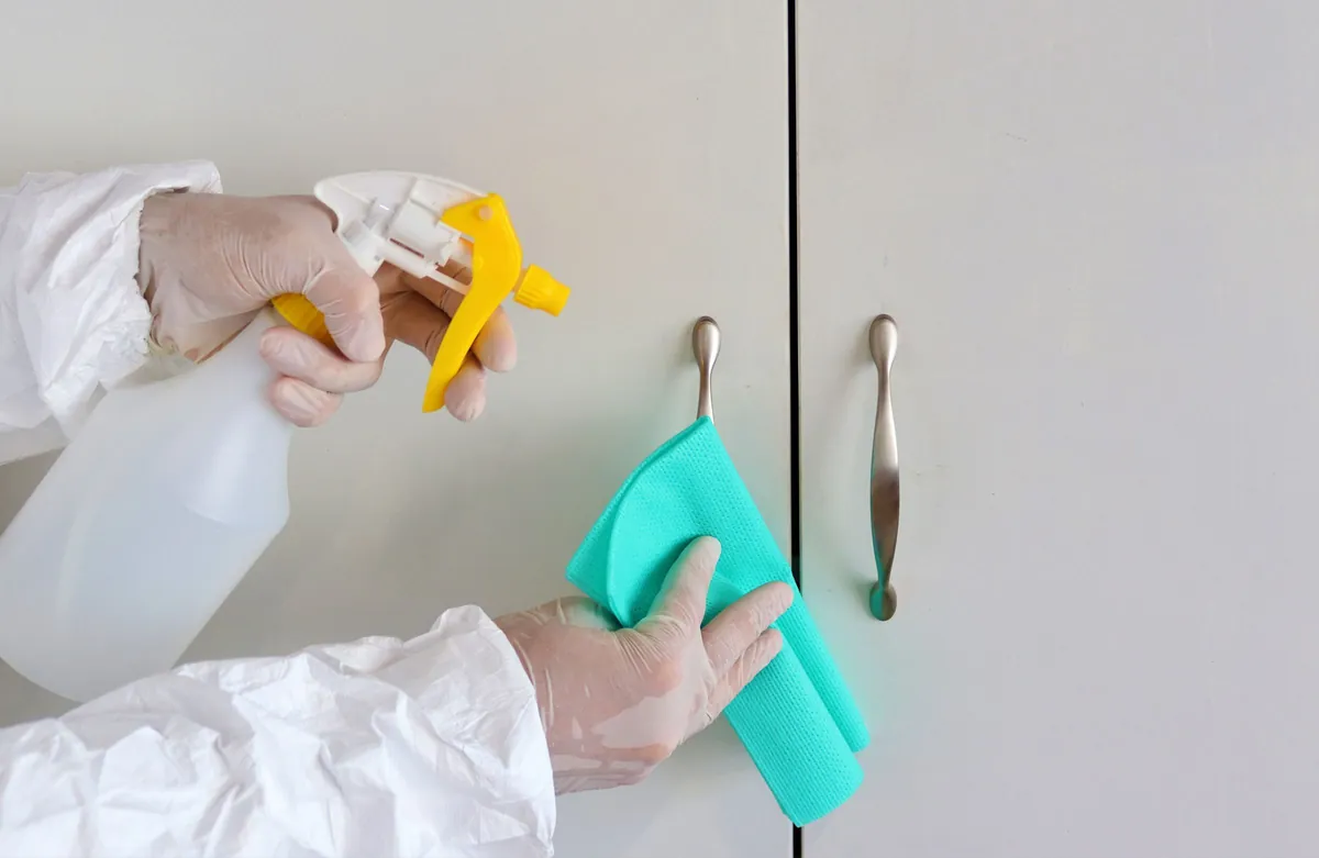 Gloved hands wiping cabinet handles with a cloth