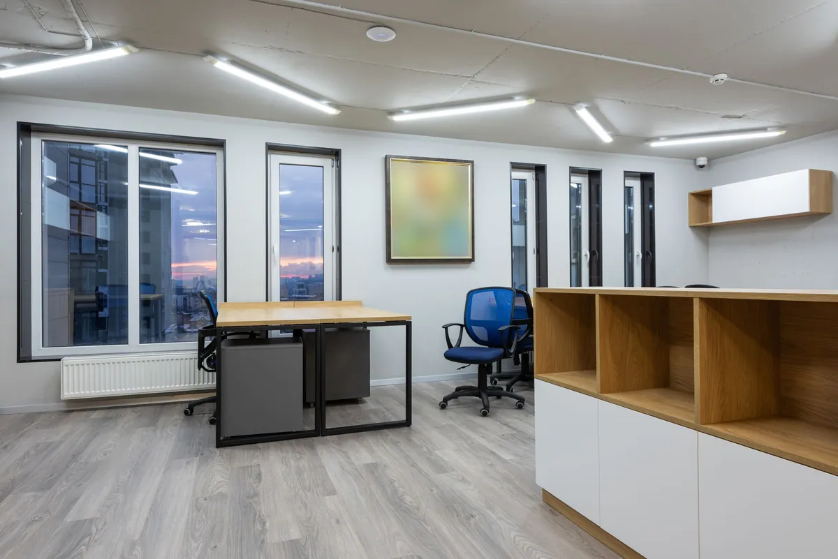 Bright open-plan office with white walls, wood desks and a blue task chair