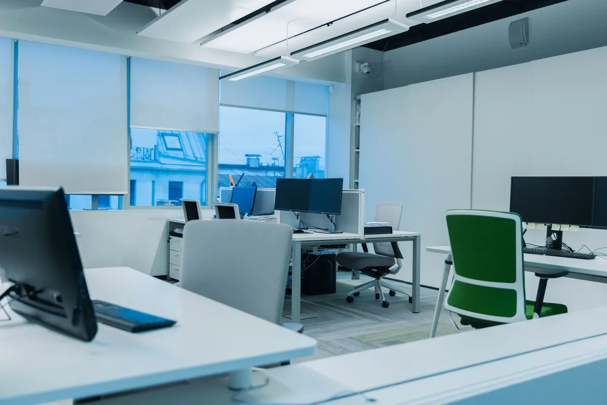 Open office with rows of monitors beside tall windows