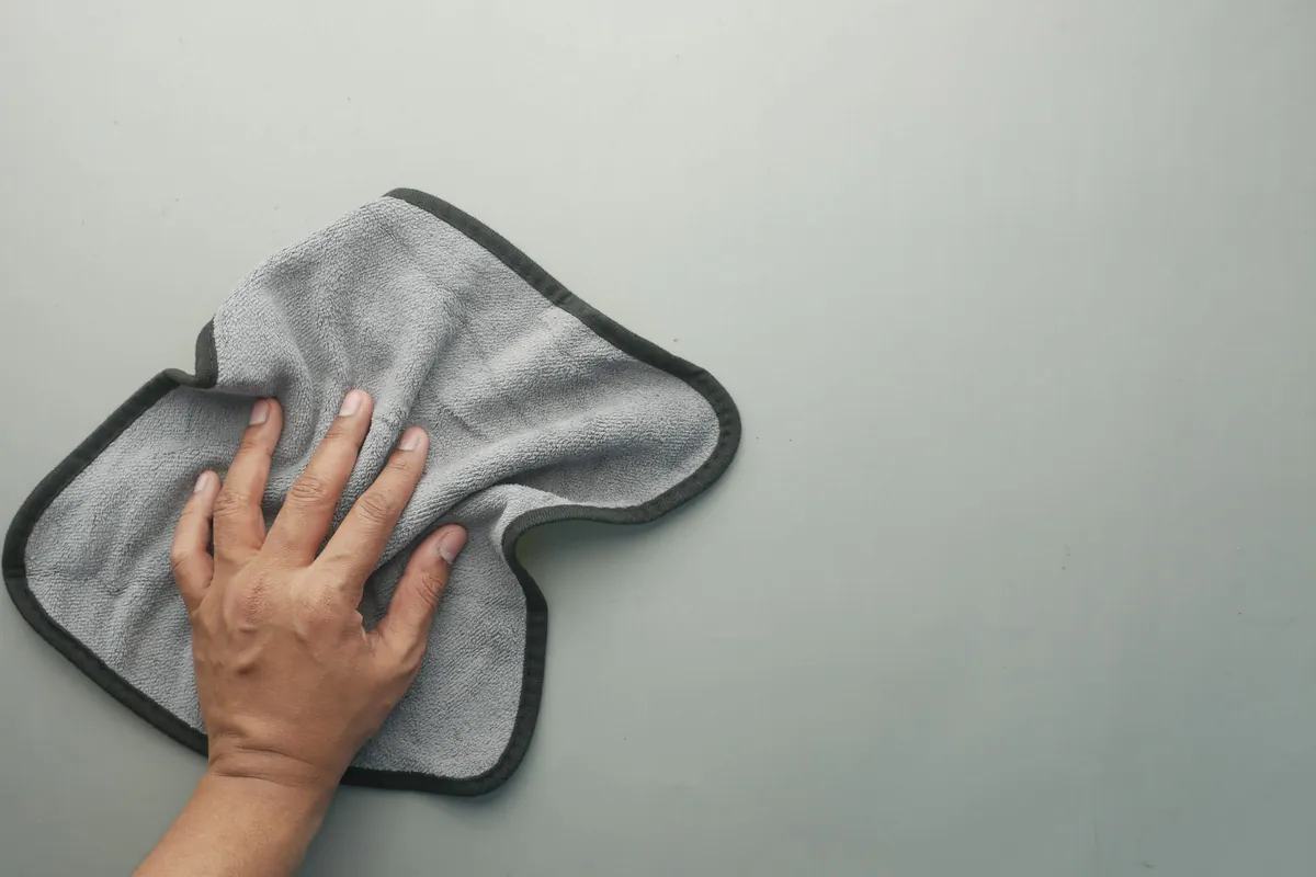 A hand wiping a surface with a gray microfiber cloth